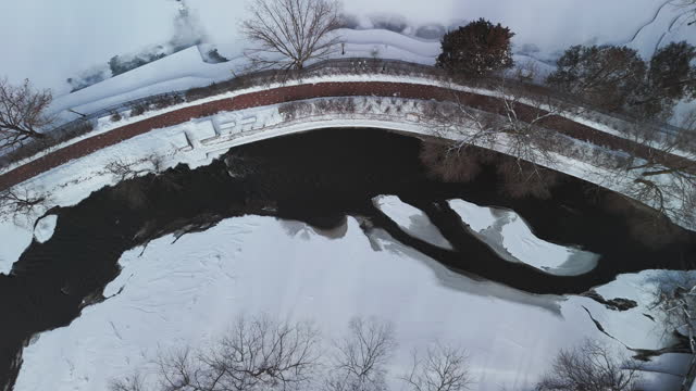 Aerial wide top down shot of a winter river, the bridge are covered with snow