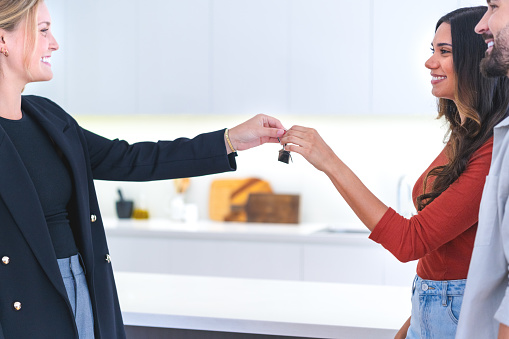 Real estate agent giving keys to a couple in a luxury home. Couple are casually dressed. They are standing in the kitchen. They are smiling and happy. Kitchen can be seen in the background