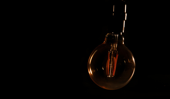 Unlit glass bulb without electricity hanging with warm reflections against black background