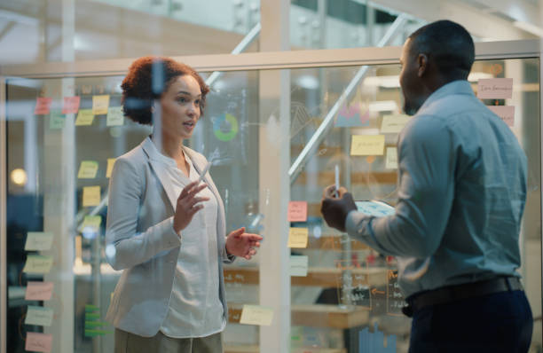 istock Planning, glass board and business people in office at night in discussion for web development research. Conversation, sticky notes and designers working with information for project in workplace. 2149038058