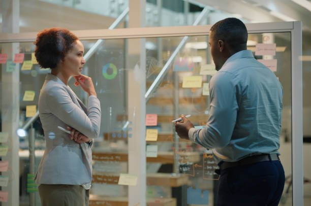 istock Business people, tablet and sticky notes on glass wall for thinking or planning, creative ideas and brainstorming. Teamwork, man and woman for sharing thoughts, strategy or entrepreneurs in office 2149038065