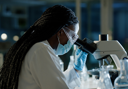 Doctor, microscope and research in lab for medical, innovation and development in vaccine study. Black woman, investigation and analysis with biotechnology for dna, healthcare exam and clinical trial