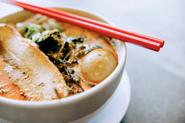 A steaming bowl of ramen noodle soup with a rich creamy broth, mushrooms, seaweed, and a soft boiled egg accompanying the pork and noodles.