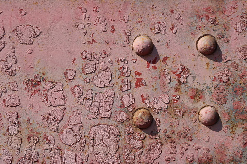 Surface of an old shabby metal wall with damaged  red paint with rivets close-up.