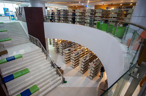 Library, research and education with books in an empty room with stairs to a floor on university or college campus. Learning, study and scholarship with book shelves in a school for development