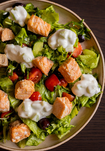 Close-up of a delicious Mediterranean salad featuring pieces of salmon fillet and a dollop of tzatziki sauce, offering a fresh and flavorful dining experience