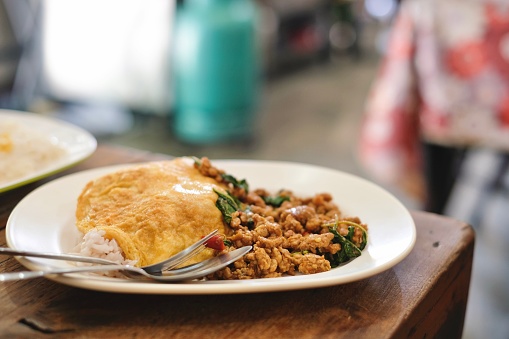 A plate of pad kra pao (holy basil pork mince stir-fry) with omelette and mixed grain rice, and a dessert of fresh mango slices with sticky rice at a street food stall in Phra Nakhon, near the Grand Palace - Bangkok, Thailand