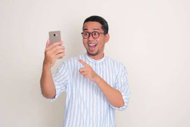 istock Adult Asian man looking and pointing to phone that he hold with wow face expression 2149047565