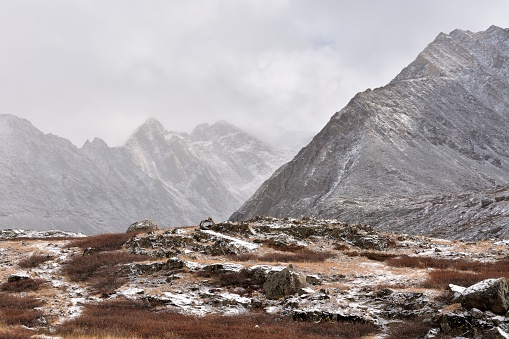 A rocky glade sprinkled with the first snow, sandwiched between two mountain ranges on a cloudy autumn morning.