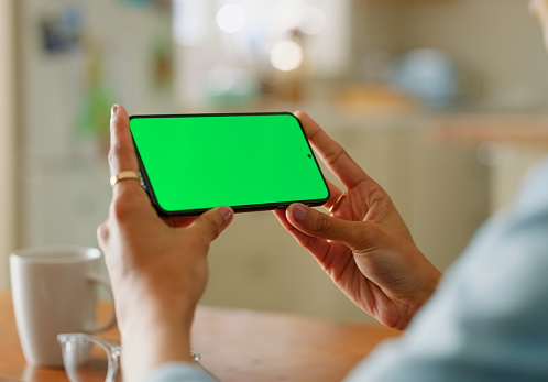 Green screen, phone and hands of woman in house streaming social media, news or video at home. Smartphone, mockup or female person with space for app, film or subscription service sign up with coffee