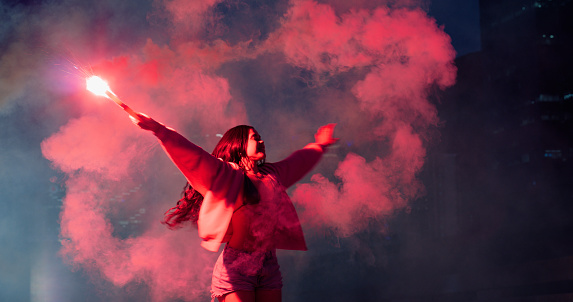 Smoke flare, color and girl holding sparks on festival, holiday and vacation for party, rave and new years eve. Lights, dance and woman with powder bomb for aesthetic, sparkle or celebrate in city