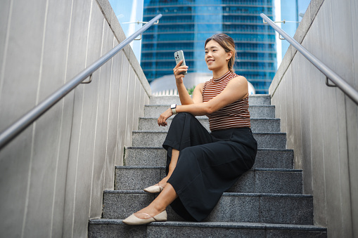 Young Asian woman looks into smartphone sitting at the stairs