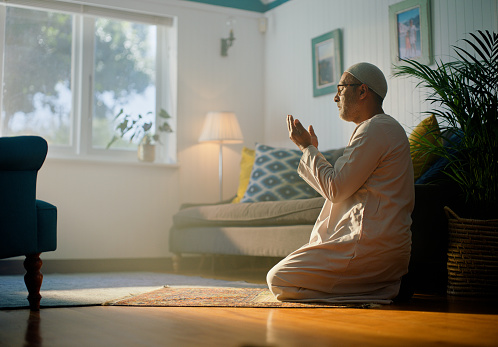 Man, God and muslim pray in house with faith, gratitude or spirituality. Islamic, religion and male person with dua prayer hands in living room with thank you, worship or respect and praise for Allah
