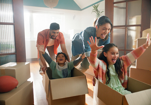 Happy family, parents and children in boxes in new home or playing game, property investment and real estate. Excited, people and moving day with fresh start and celebration for bond payment on house