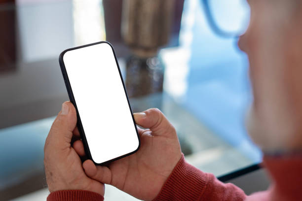 istock Older man in living room holding cell phone with blank screen. 2149056714