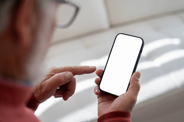 istock Older man in living room holding cell phone with blank screen. 2149056717