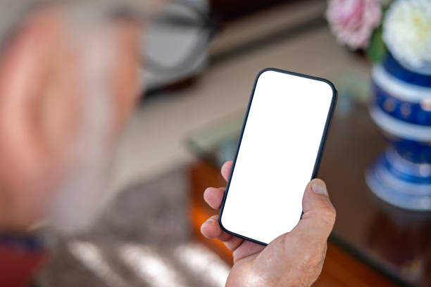 istock Older man in living room holding cell phone with blank screen. 2149056721