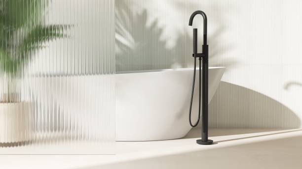 istock Freestanding white ceramic bathtub, black floor shower head, tropical palm tree with reeded glass partition in sunlight 2149057393