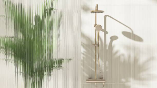 istock Gold rain shower, adjustable shower head, green palm tree, reeded fluted glass partition in sunlight on cream wall bathroom 2149057398