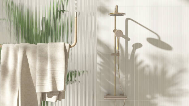 Gold rain shower, adjustable shower head, green palm tree, reeded fluted glass partition in sunlight on cream wall bathroom