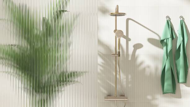 istock Gold rain shower, adjustable shower head, green palm tree, reeded fluted glass partition in sunlight on cream wall bathroom 2149057404