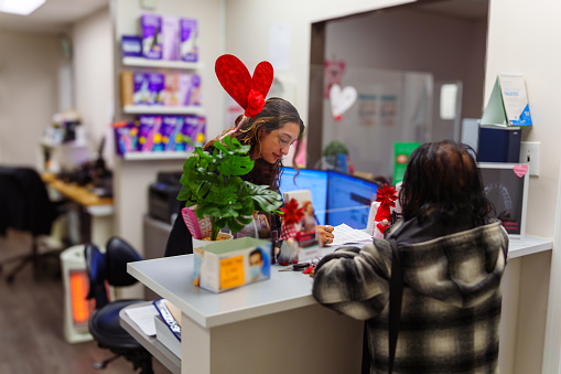 A female adult patient stands at the secretary's counter, checking in for an appointment inside a dental office.