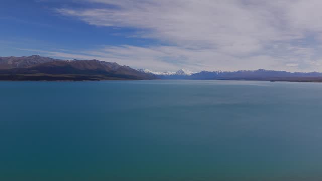 Establishing drone shot of Lake Pukaki with Mount Cook and Mount Aoraki. Driving cars on coastal road at sunny day. Stunning landscape of New Zealand. Wide shot.