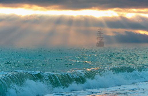 Sailing old ship in a storm sea in the background stormy clouds at sunset