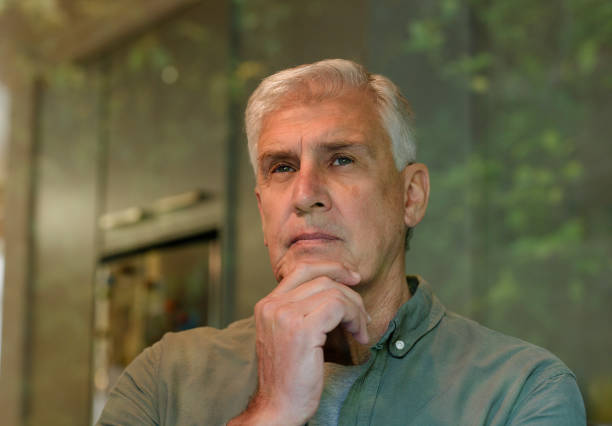 Home, thinking and mature man at window with memory, idea or insight for planning, vision or mindset. Reflection, glass and male person in apartment with choice, decision or peace on weekend morning