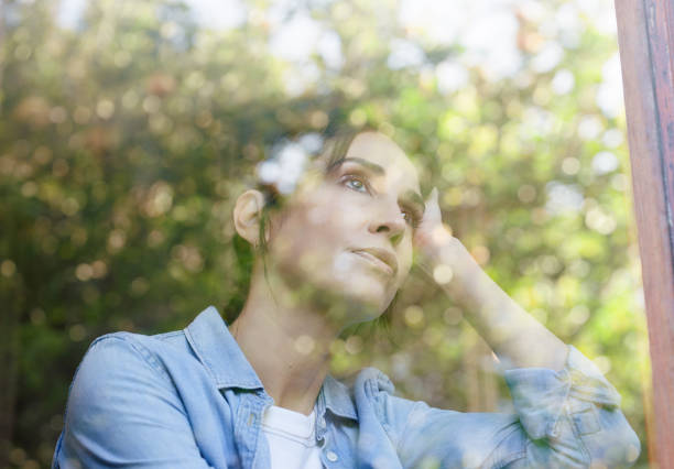 Home, thinking and woman at window with memory, idea or insight for planning, vision or mind. Reflection, glass and female person in apartment with mental health, remember or sad on weekend morning