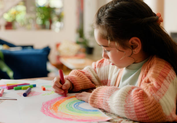 Girl, child and drawing with rainbow in home for development, learning and creativity with paper at desk. Kid, sketch and crayon for skills, art and color with pattern for progress in family house