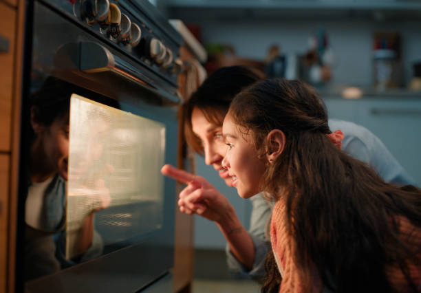 Mom, girl and check oven in kitchen for baking, cake or muffins with pointing, learning and teaching. Stove, mother and daughter with support, bonding and love with smile for food in family house