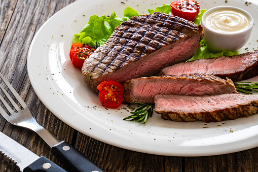 Grilled beef sirloin steak with fresh vegetables on wooden background