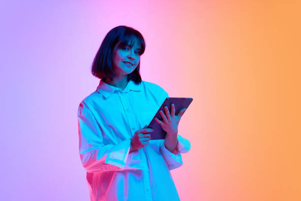 istock Young woman with short haircut looking at camera during using digital tablet in neon light against gradient studio background. 2149065994