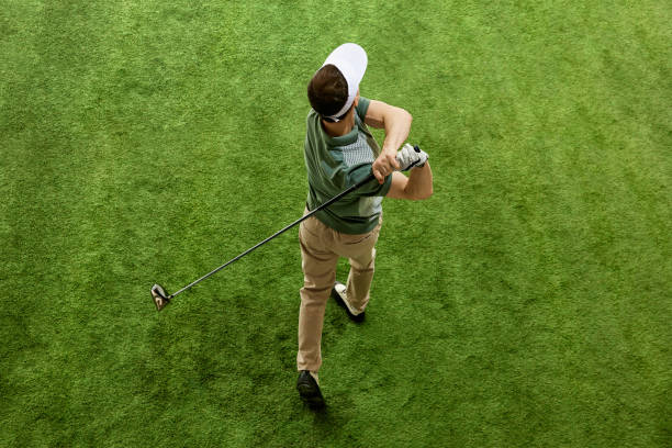 High overhead angle view of skilled golfer in casual attire hitting golf ball on fairway green grass. Concept of recreation, sport games. High overhead angle view of skilled golfer in casual attire hitting golf ball on fairway green grass. Concept of professional sport, luxury games, active lifestyle, action. Ad golfer swinging club stock pictures, royalty-free photos & images