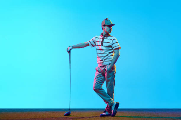 Young man, golf player in retro attire nd cap posing with golf club in neon light against gradient blue background. Young man, golf player in retro attire nd cap posing with golf club in neon light against gradient blue background. Concept of professional sport, luxury games, active lifestyle, action. Ad golfer swinging club stock pictures, royalty-free photos & images