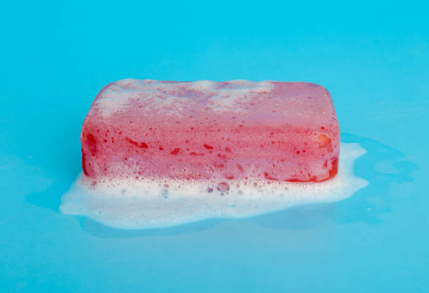 Red Soap Bar, Body Care Cosmetic, Fruit Flavored Soapy Detergent, Solid Shampoo, Red Translucent Glycerin Soap on Blue Foamy Background