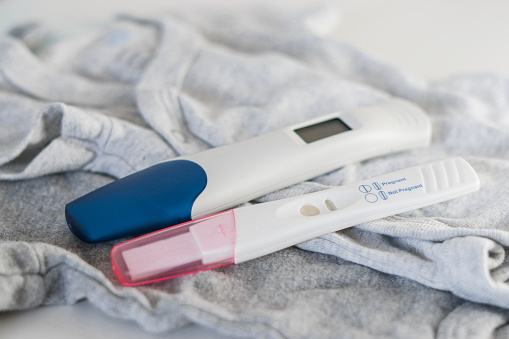 Top view of two positive pregnancy tests on baby clothes, white table