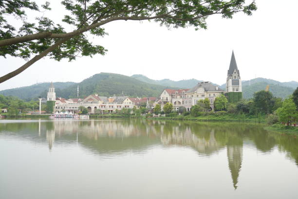 A stunning church with tall spires stands next to a tranquil lake, surrounded by lush greenery and colorful trees.
