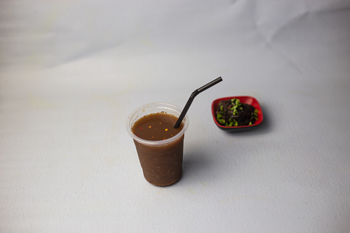 Tetul Juice or Tamarind water with straw served in disposable glass isolated on grey background side view of healthy organic drink
