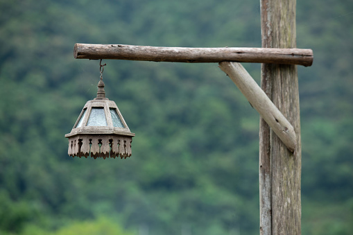 Thai traditionan wooden lantern hang on wooden post with green blurred background.