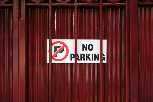 No parking, sign on a dark red metal fence with bars.