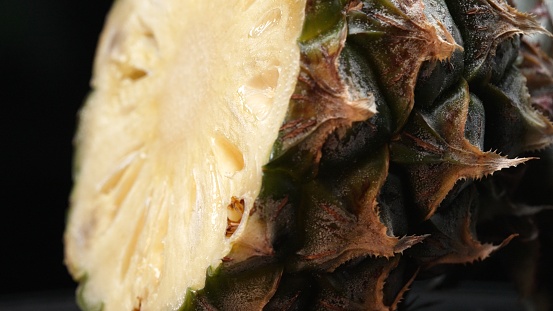 Macrography of a fresh pineapple cut in half takes center stage against a sleek black background. Each close-up shot captures the intricate details and textures of the pineapple. Close up. Comestible.