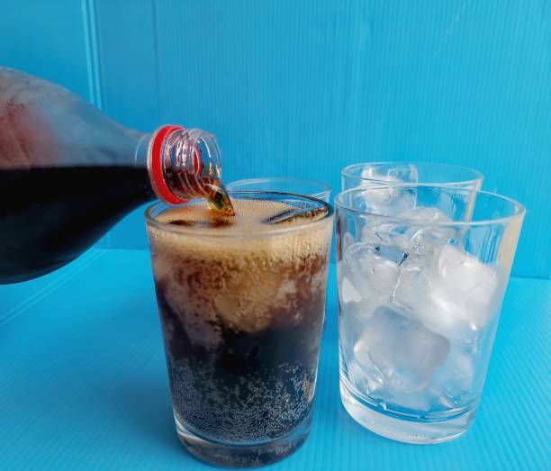 istock Pouring cola drink on glass with ice cubes on blue background 2149074266