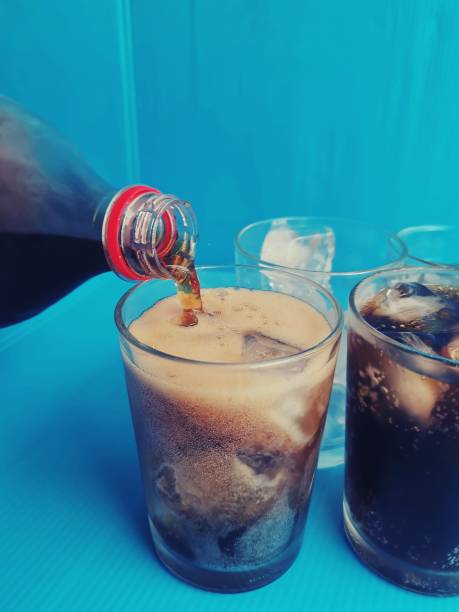 istock Pouring cola drink on glass with ice cubes on blue background 2149074282
