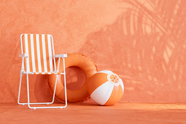 オレンジ色の背景にビーチチェアとインフレータブルリングと夏のビーチホリデー旅行の背景
