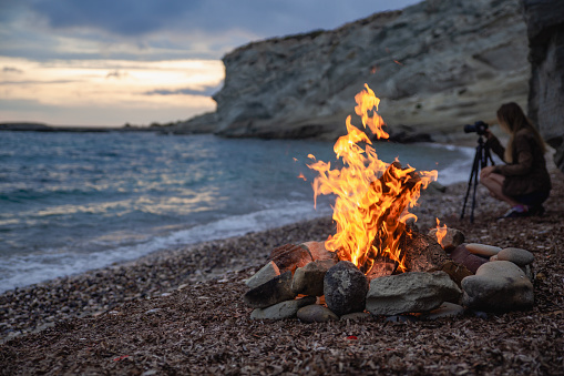 Woman photographer with professional camera landscape sunset Campfire on the beach.