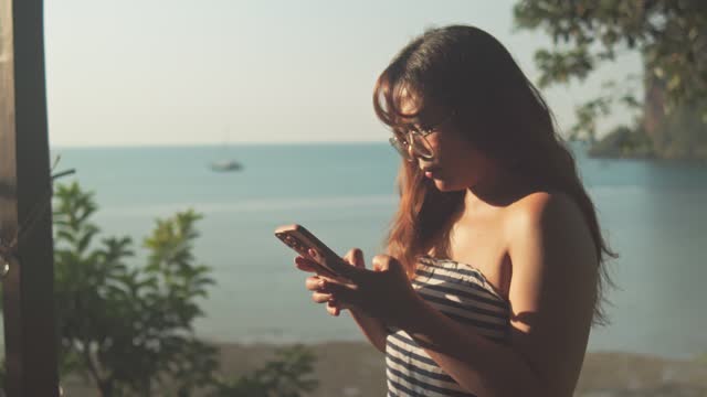 Young Woman Using Smartphone with Tropical Ocean View in Background.