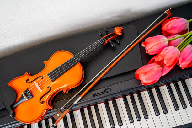 an elegant violin, a bow and a bouquet of red tulips with delicate petals lie on the piano, a beautiful composition