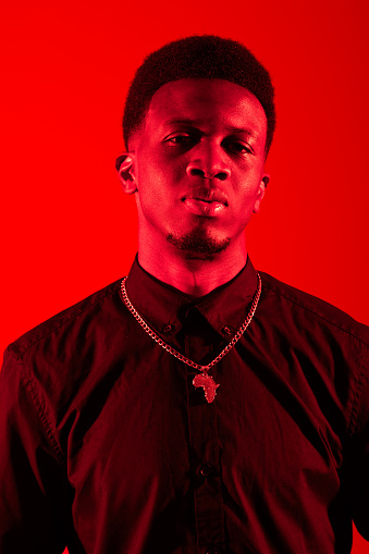 A black man standing confidently in front of a vibrant red background in a studio setting.